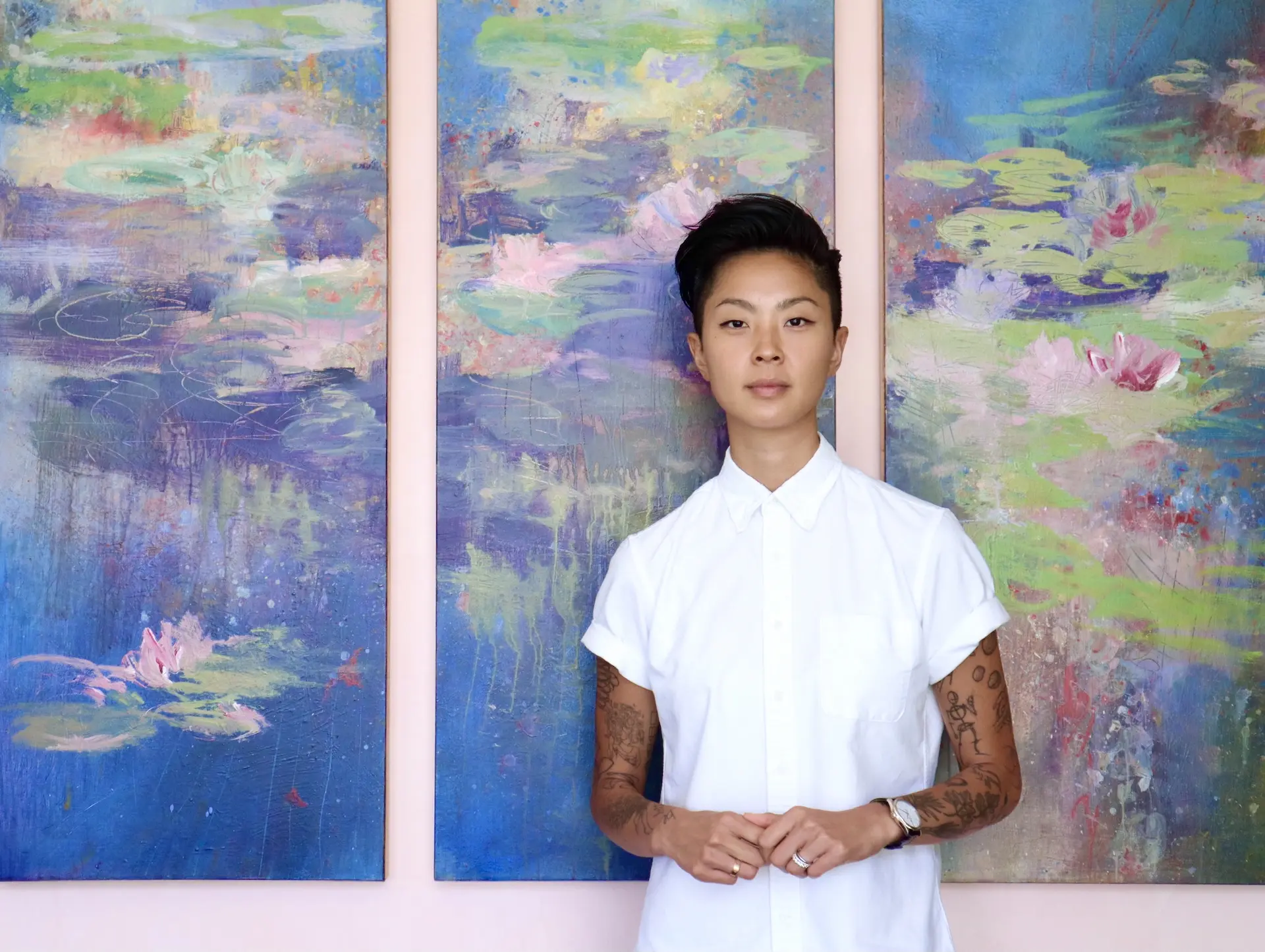 A person wearing a white collared shirt is standing in front of a painted tapestry and a pink wall.