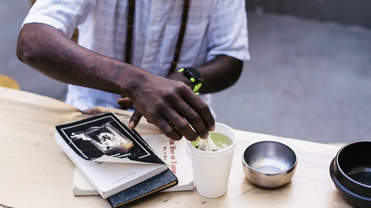Man hands stirring the green tea on the table with books and empty bowl