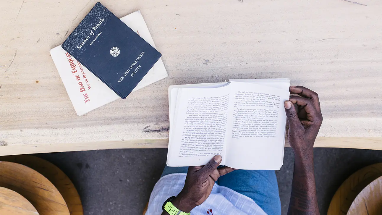 Man hand holding the open book with two books kept on the table
