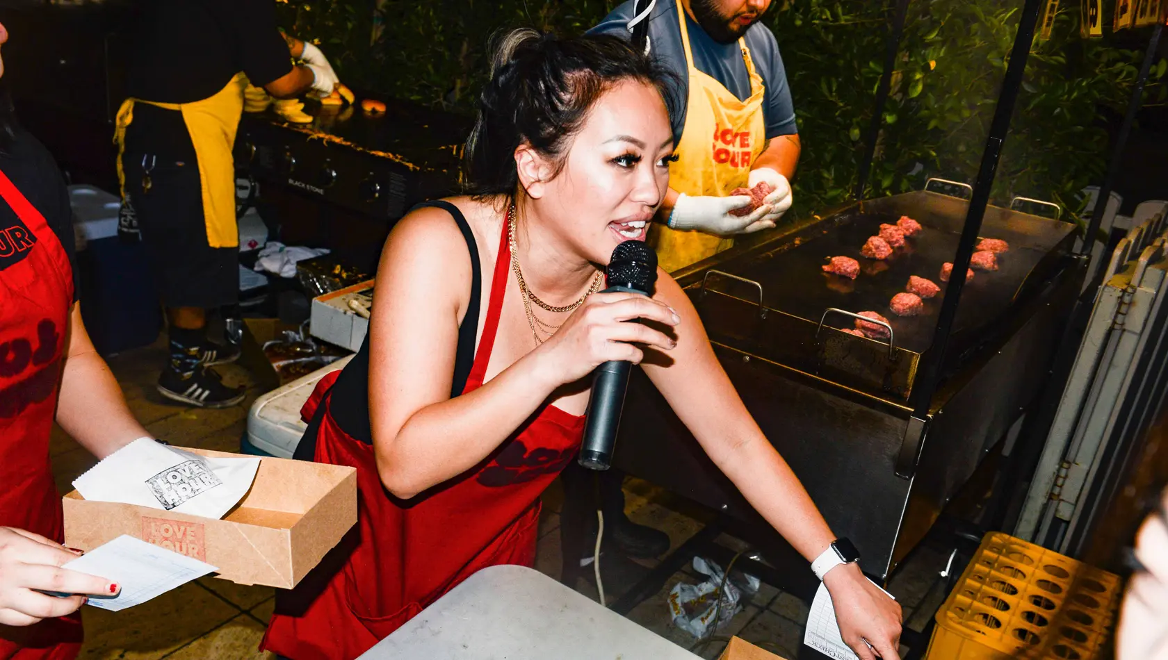 Girl holding mic and singing and man in the background cooking food