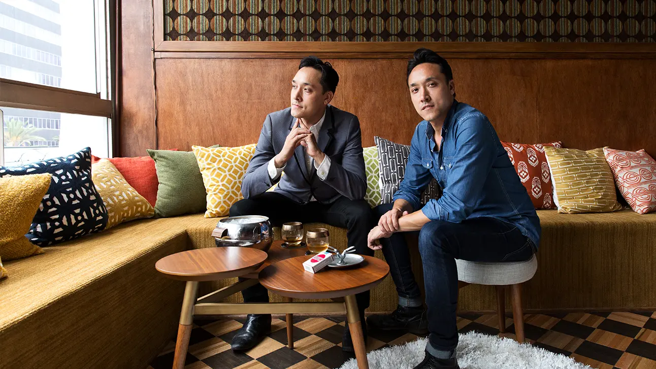 Two man sitting in a sofa posing with a transparent glass window