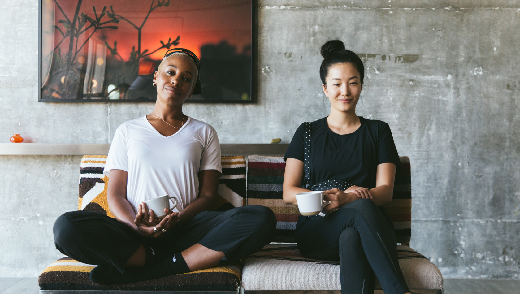Two girls smiling and sitting on a sofa with the cup of coffee