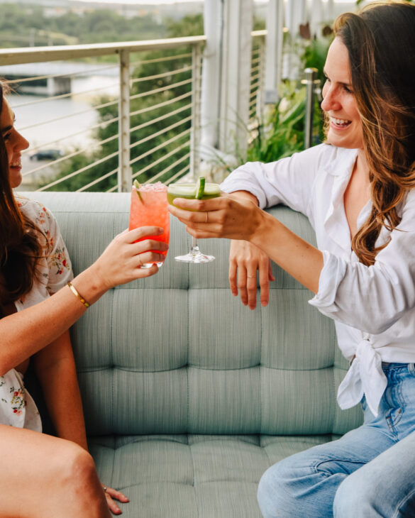 Two girls cheers with the cup of juice sitting in balcony