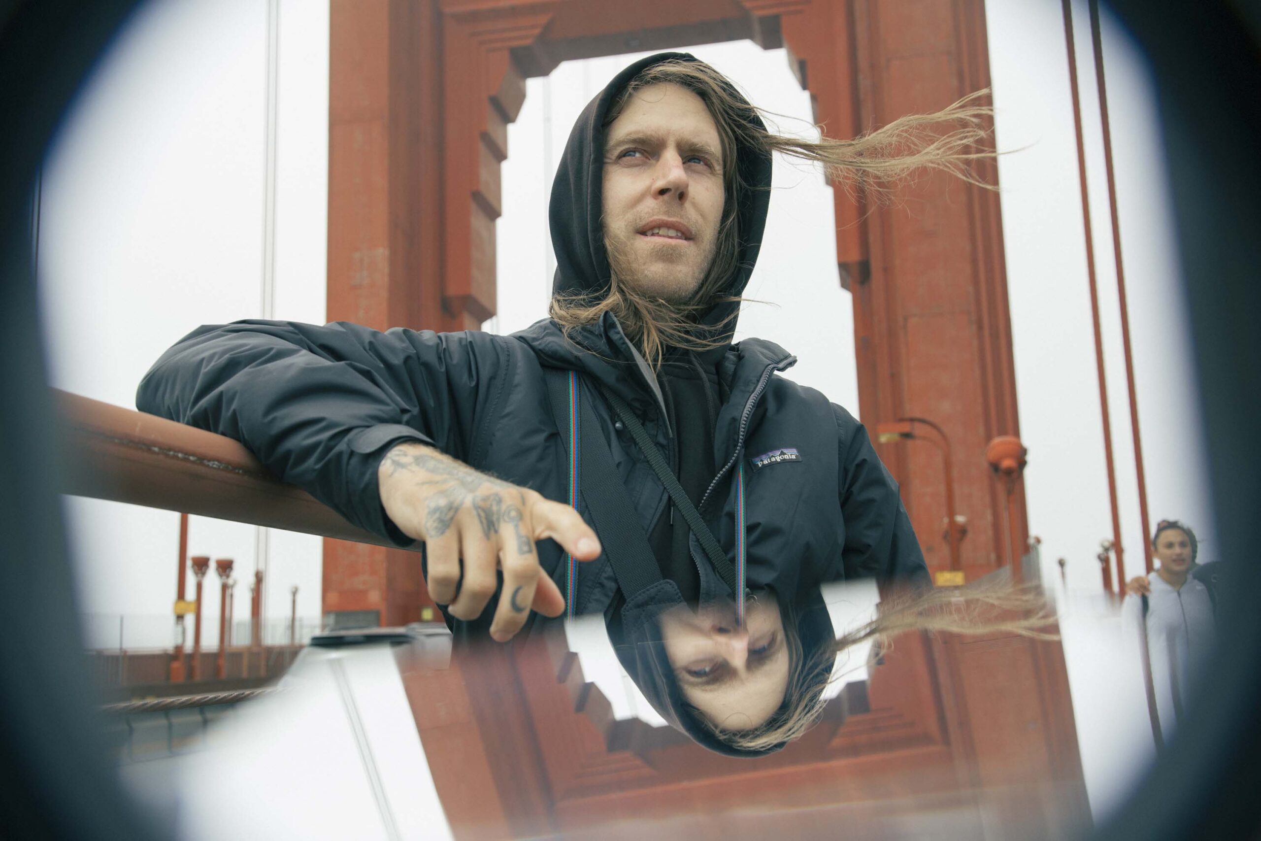 A man wearing a hoodie looks out while standing on a red bridge.