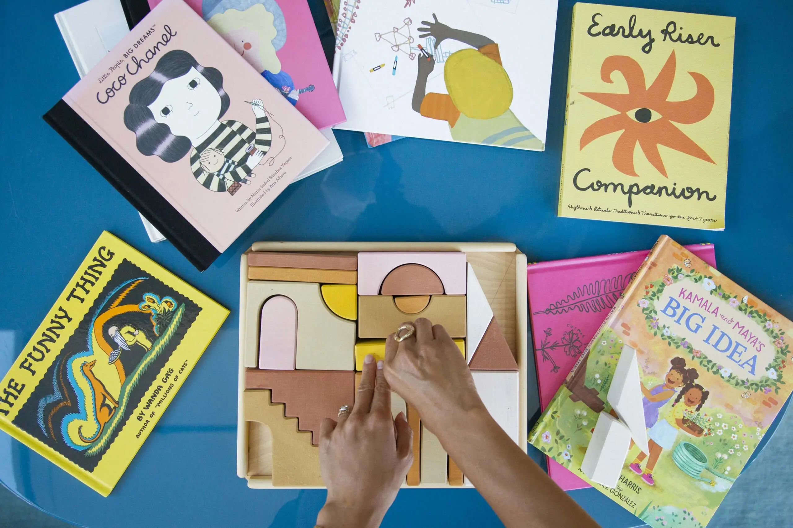 Two hands are arranging a wooden puzzle for children, and there are books surrounding the puzzle.