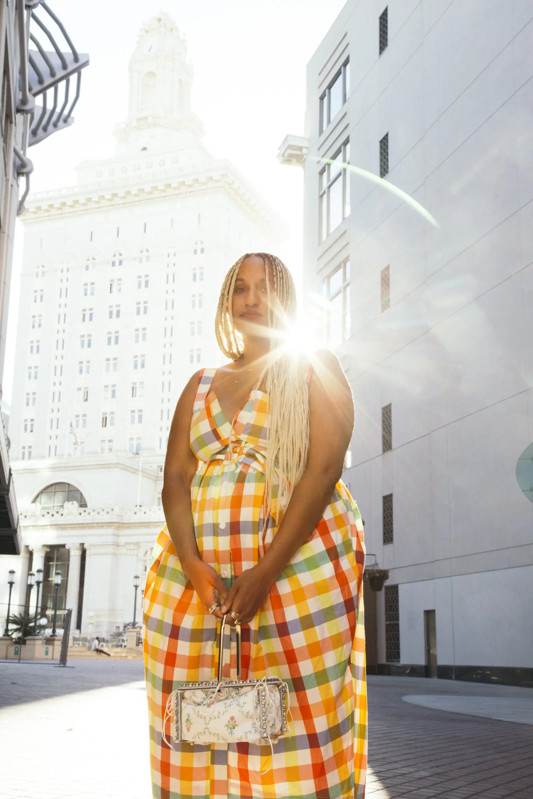 A woman wearing a gown dress is holding a handbag and posing for a picture in front of a beautiful architectural building.