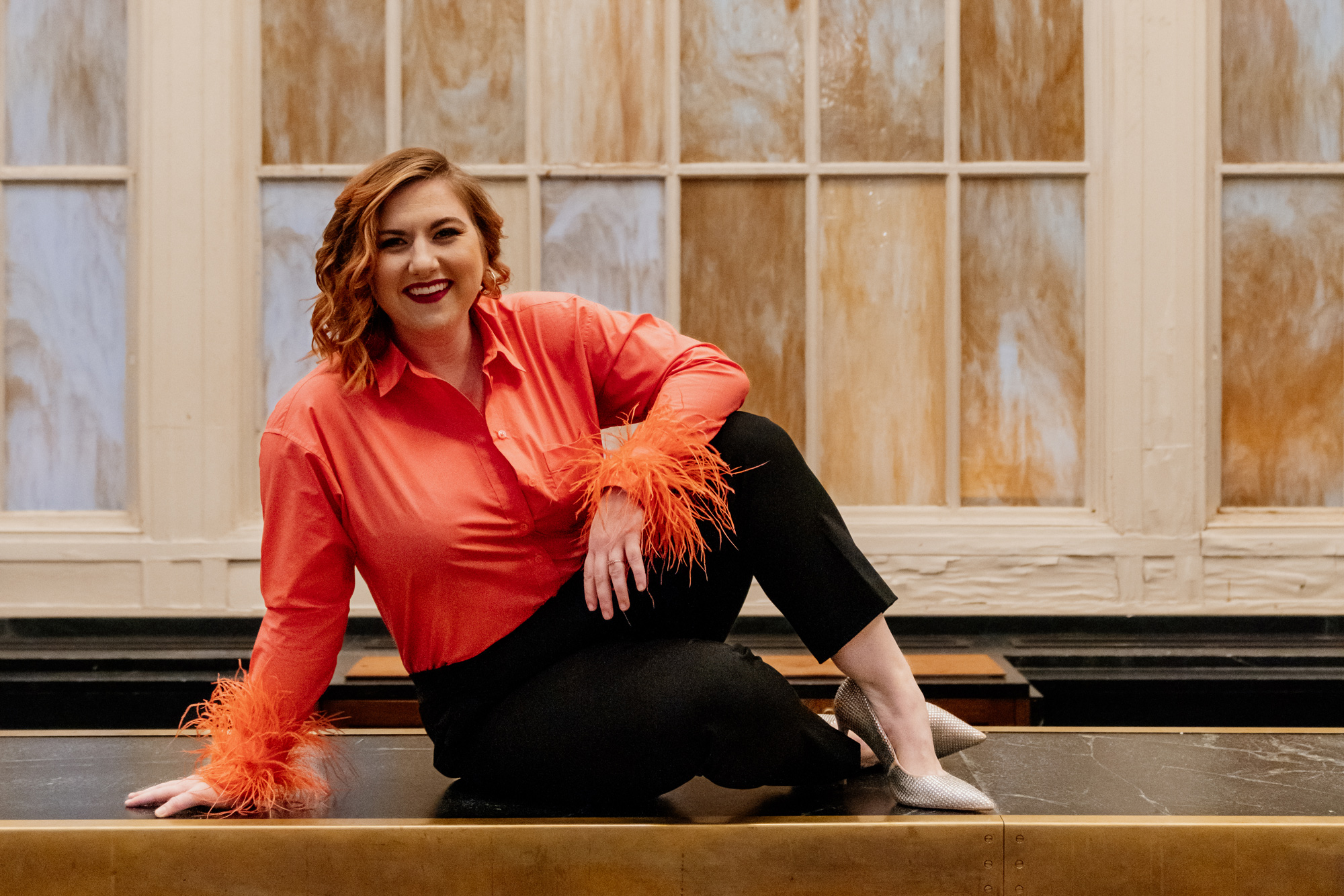 Redheaded woman in a coral shirt poses on a countertop