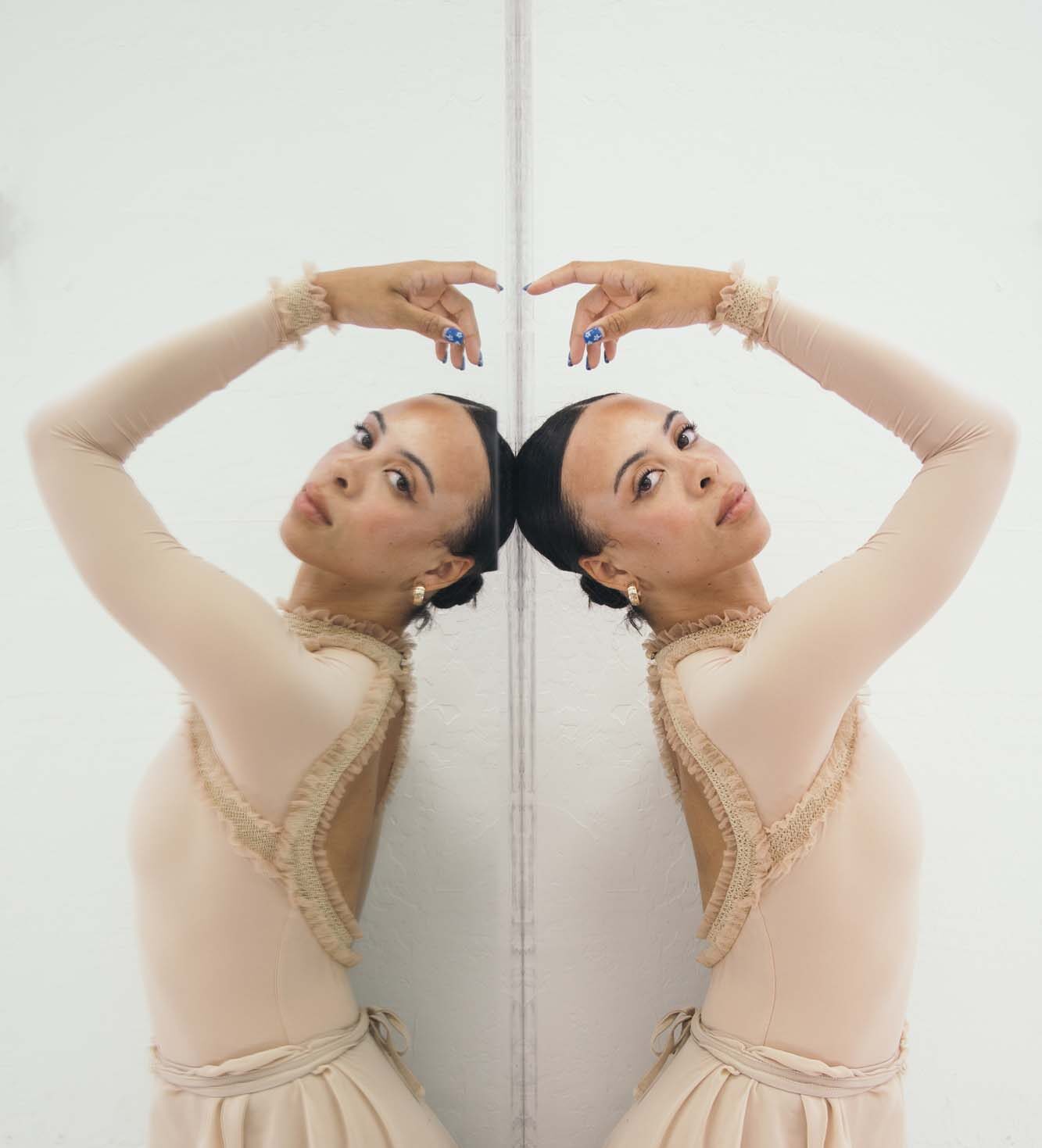 A dancer is posing for a picture while looking directly at the camera, and her image is perfectly reflected in a mirror.