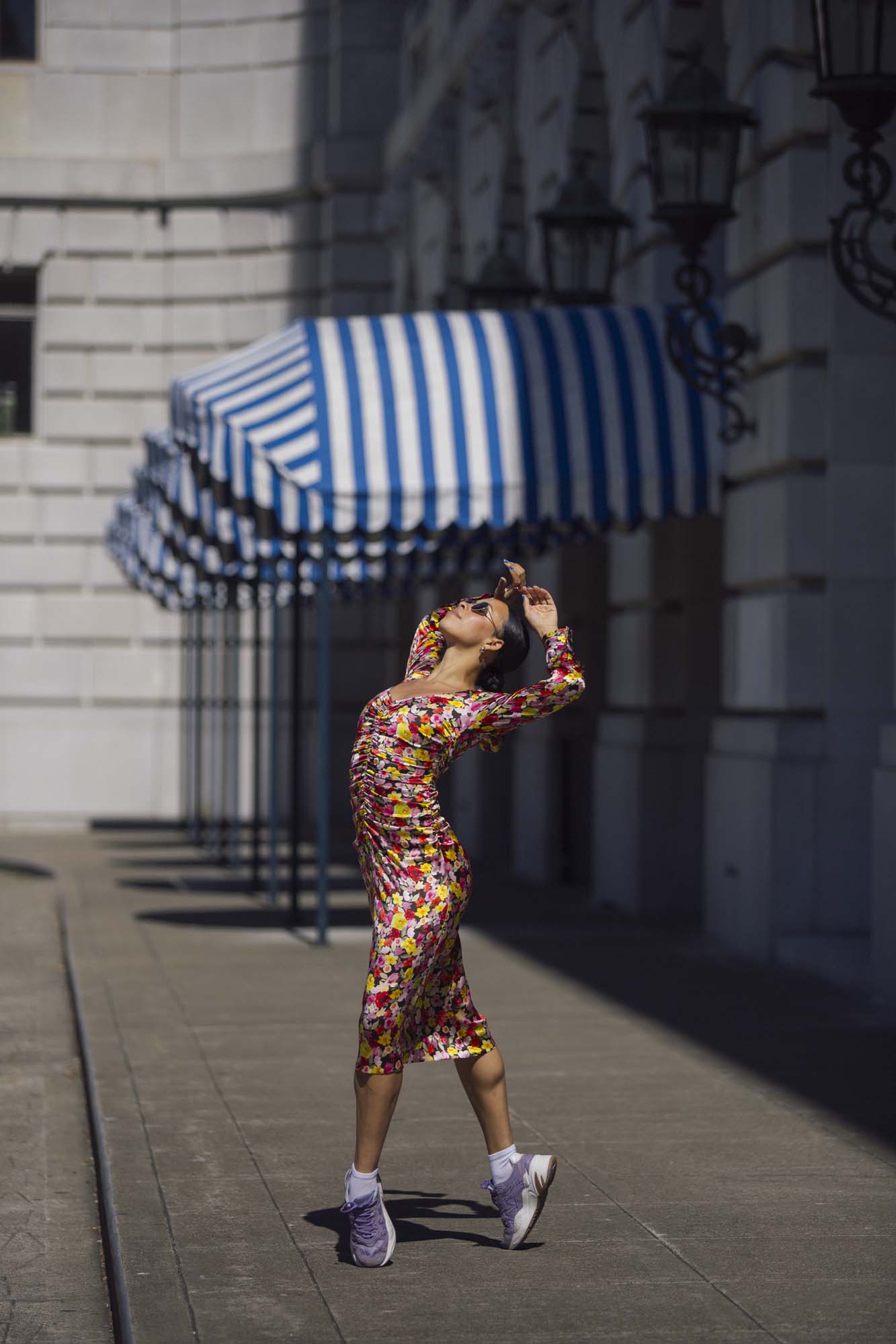 A woman wearing a floral dress and sports shoes is posing for a picture.