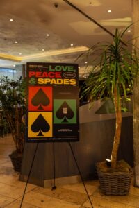 A sign for a game night called Love Peace & Spades stands next to a potted plant