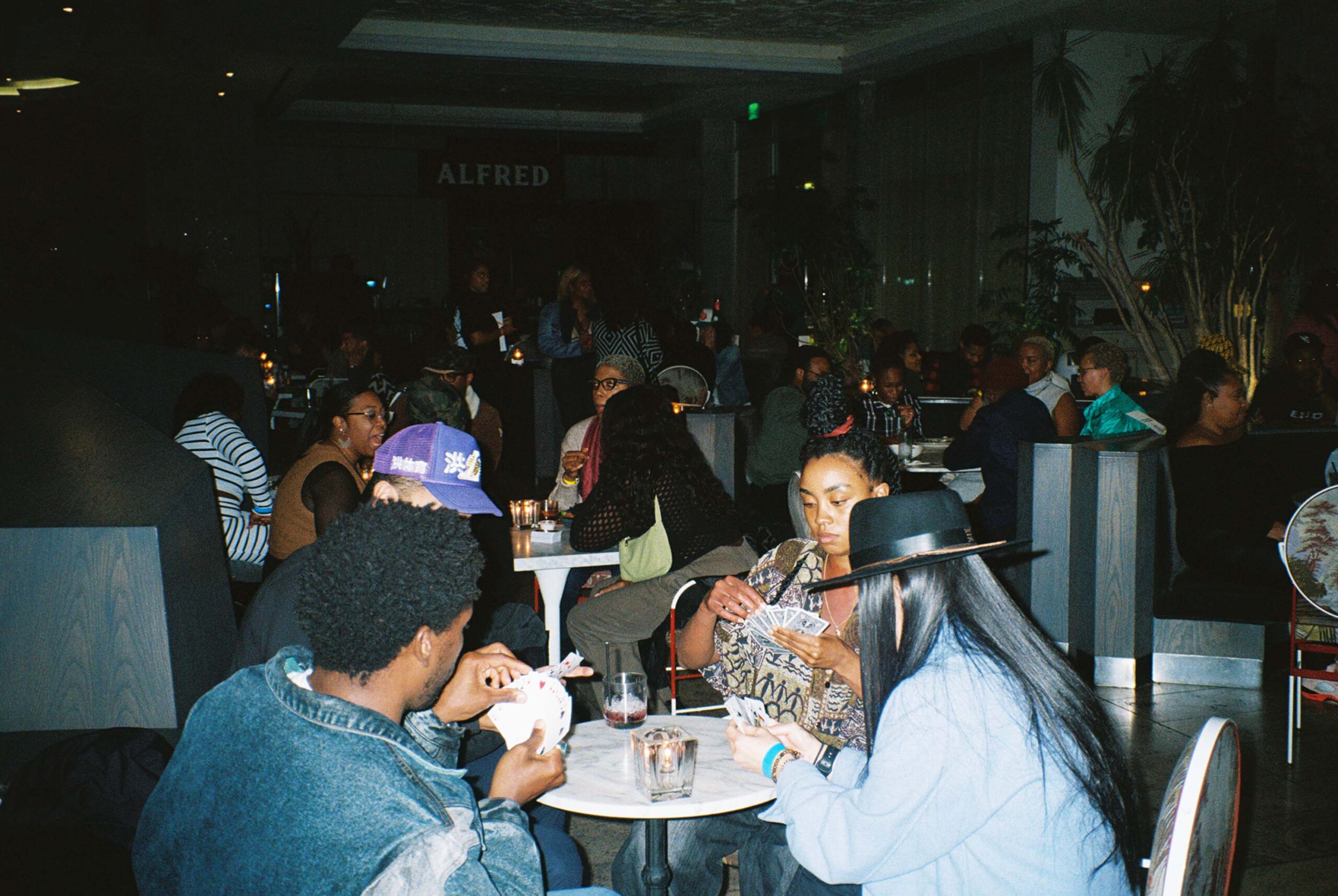 Card players sit around a small table in a room full of people for a card night