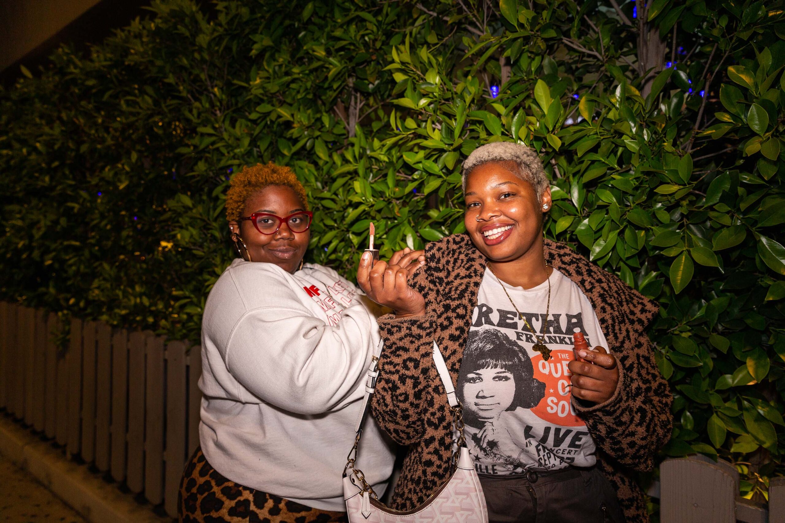 Two ladies pose for a click, one holding lipstick, enjoying a delightful evening together.