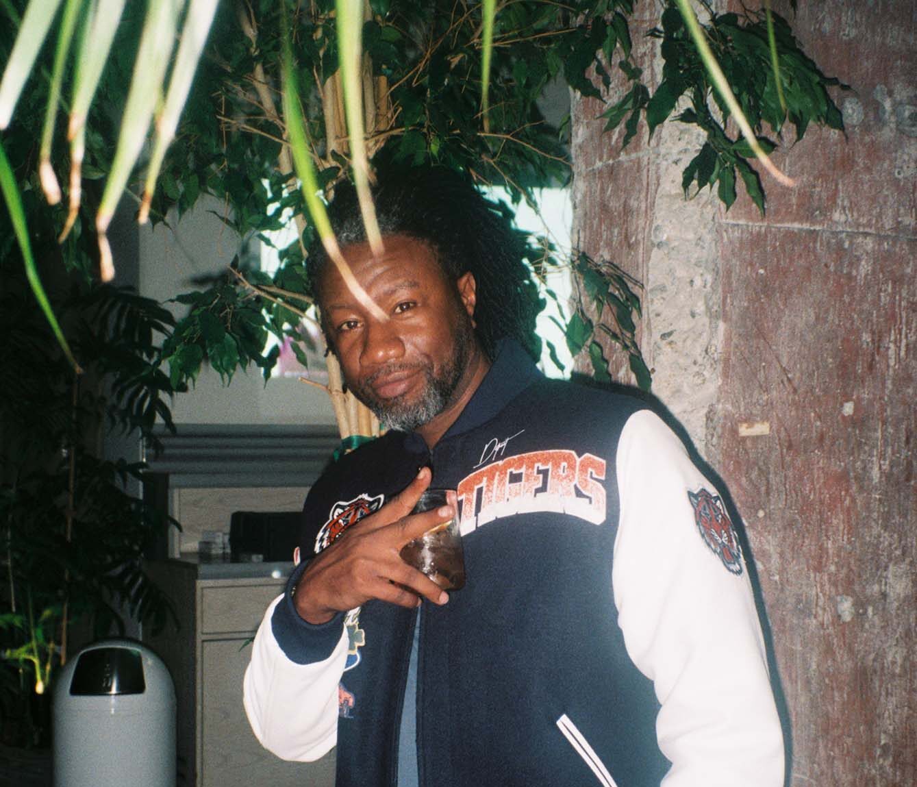 A man in a jacket poses while giving a sideways peace sign