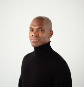 A man in a black turtleneck looks at the camera