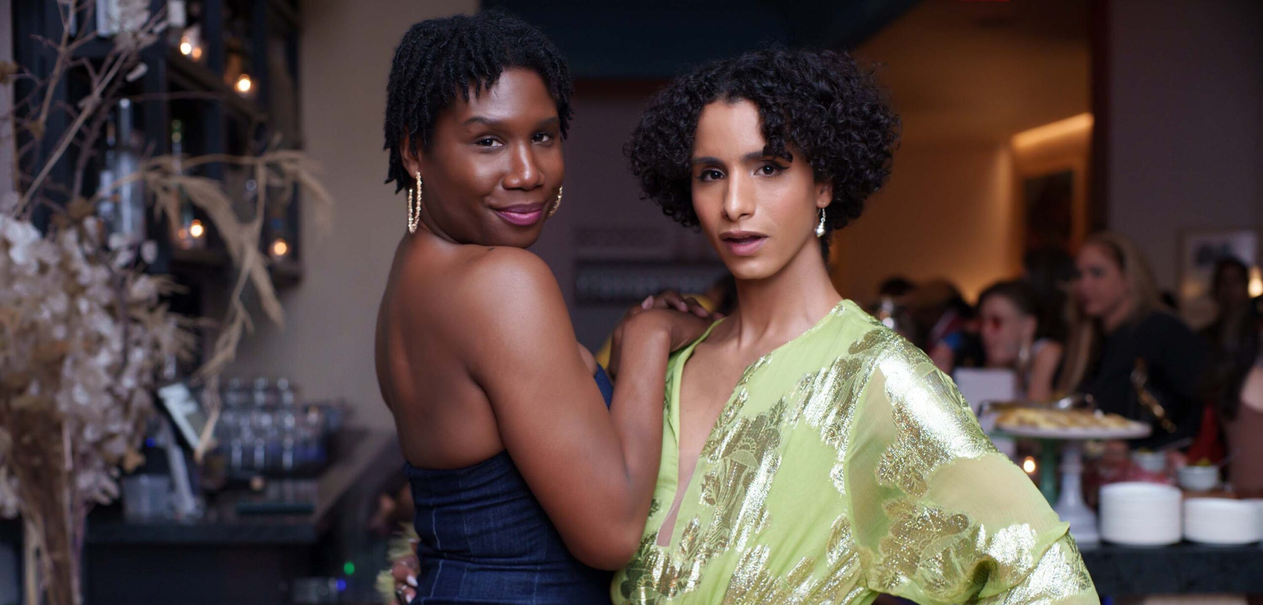 Two women in dresses embrace each other and pose