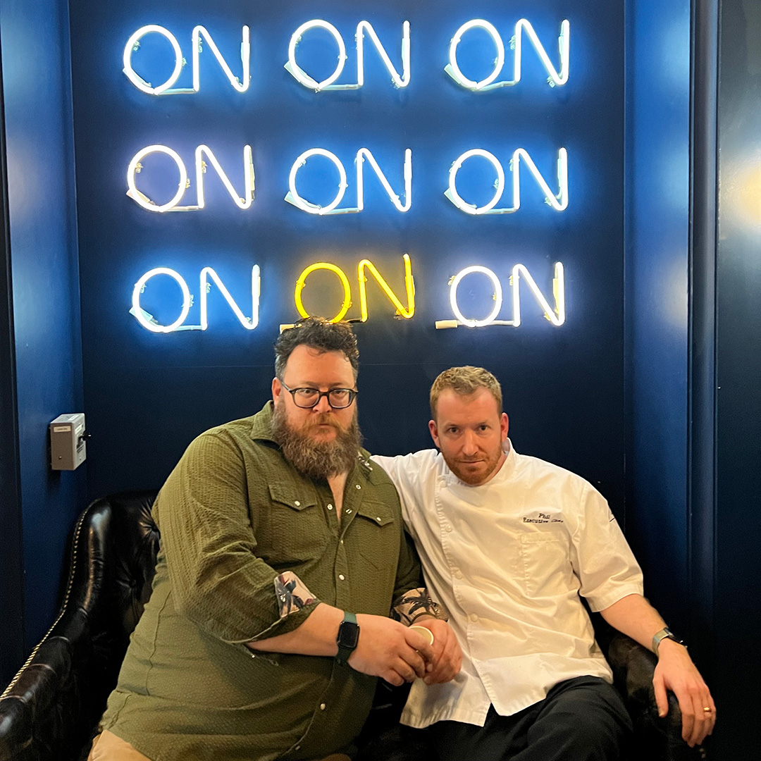 Lukas B Smith and Chef Phil Marzelli - two men sitting together in front of a neon sign