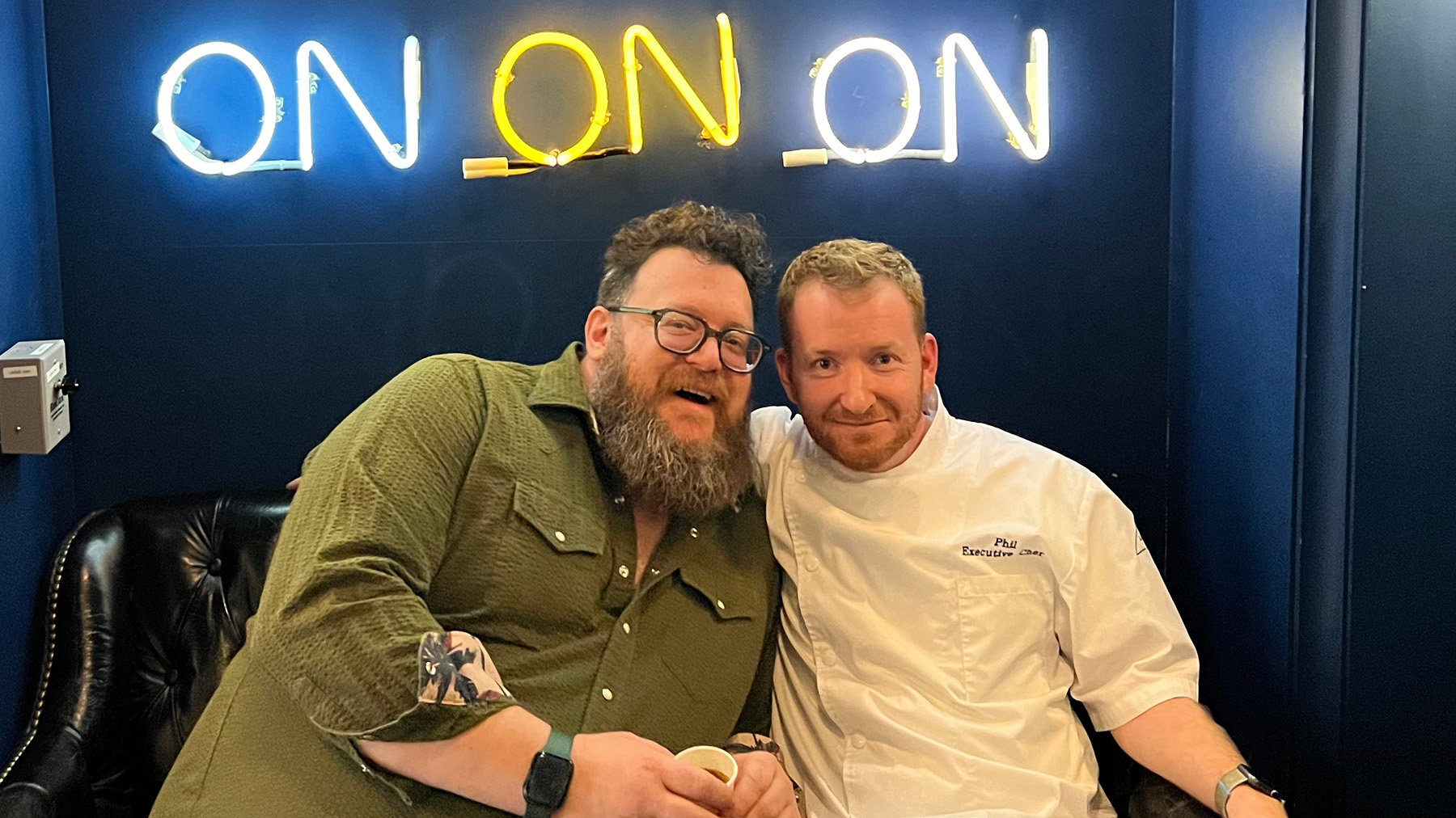 Lukas B Smith and Chef Phil Marzelli - two men sitting together in front of a neon sign
