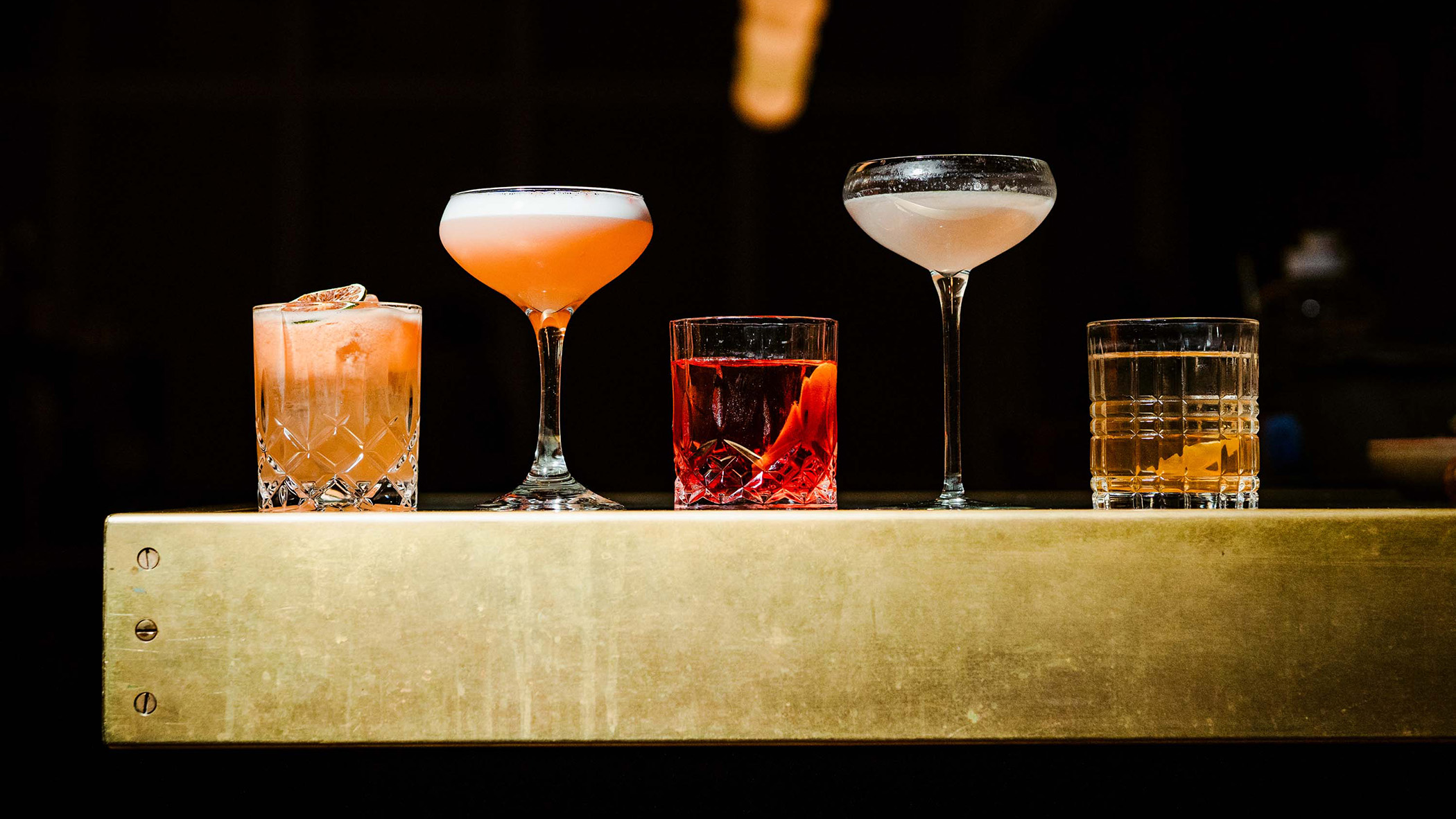 five cocktails in varying color and glasses at No Goodbyes