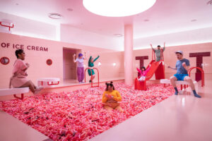People playing in a pink ice cream sprinkle pit with slides and benches.