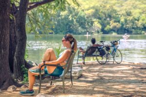 Woman relaxing on lakeside bench in athletic wear, with cyclists and paddlers nearby.
