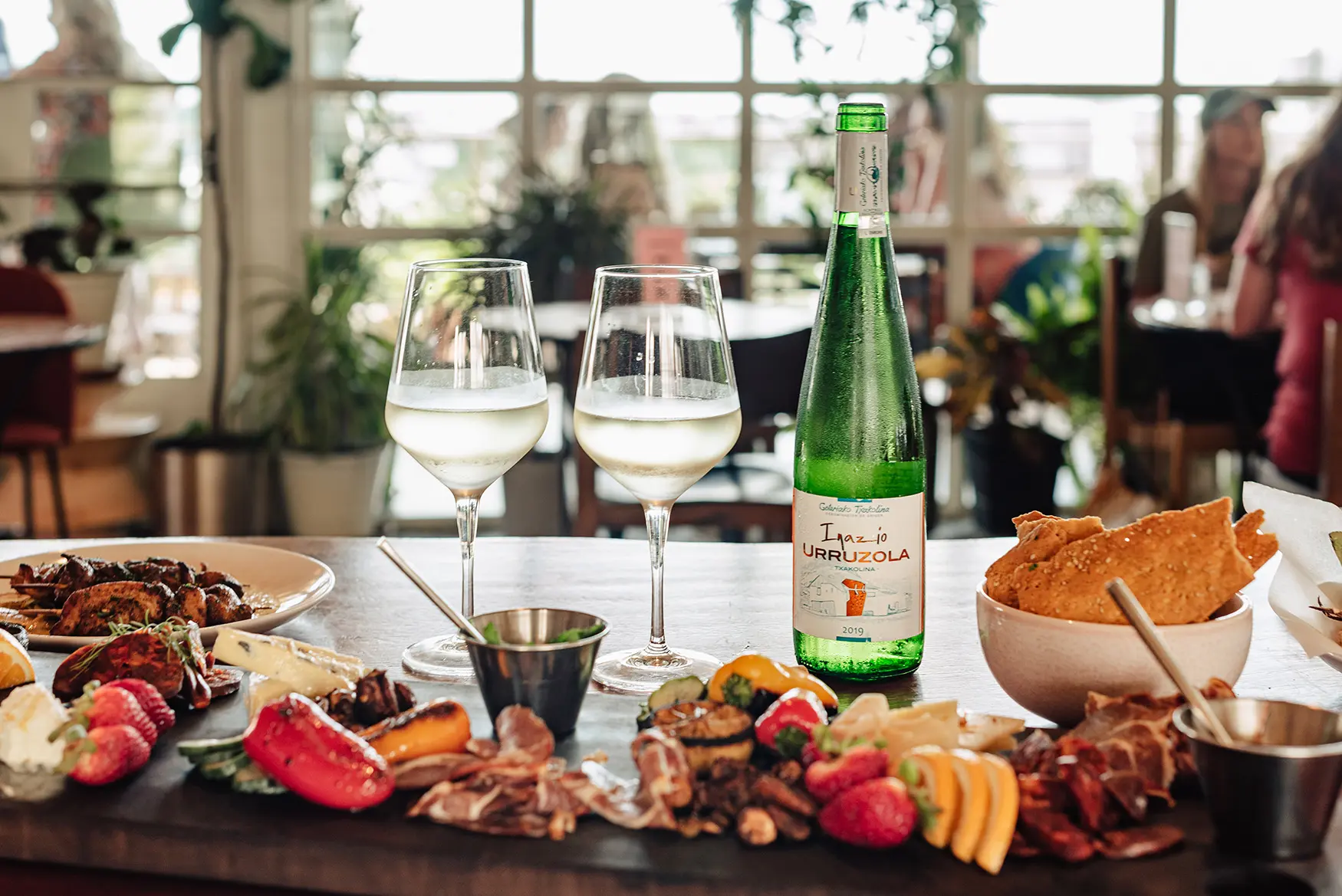 Charcuterie board with assorted meats, fruits, cheeses, two wine glasses, green bottle on a dining table.