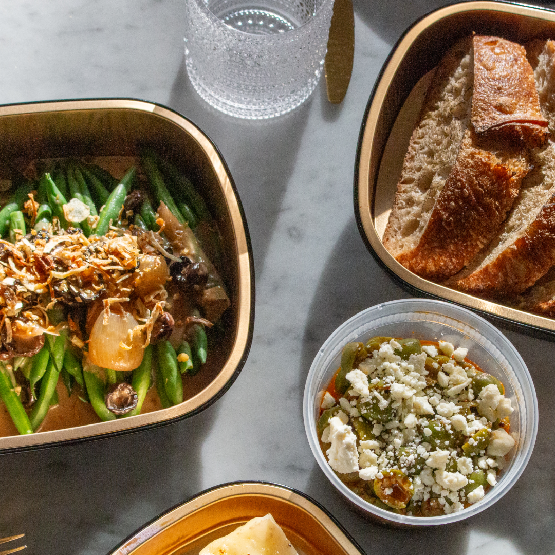 A meal spread with green beans, toasted bread slices, feta salad, and lasagna on marble table.