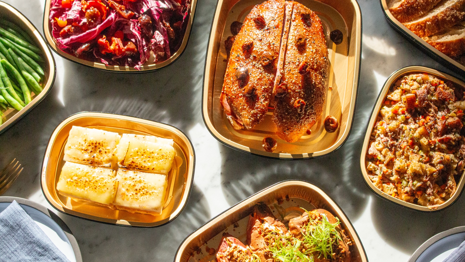 Golden roasted meat with herbs, sauce, and side dishes on sunlit marble table.