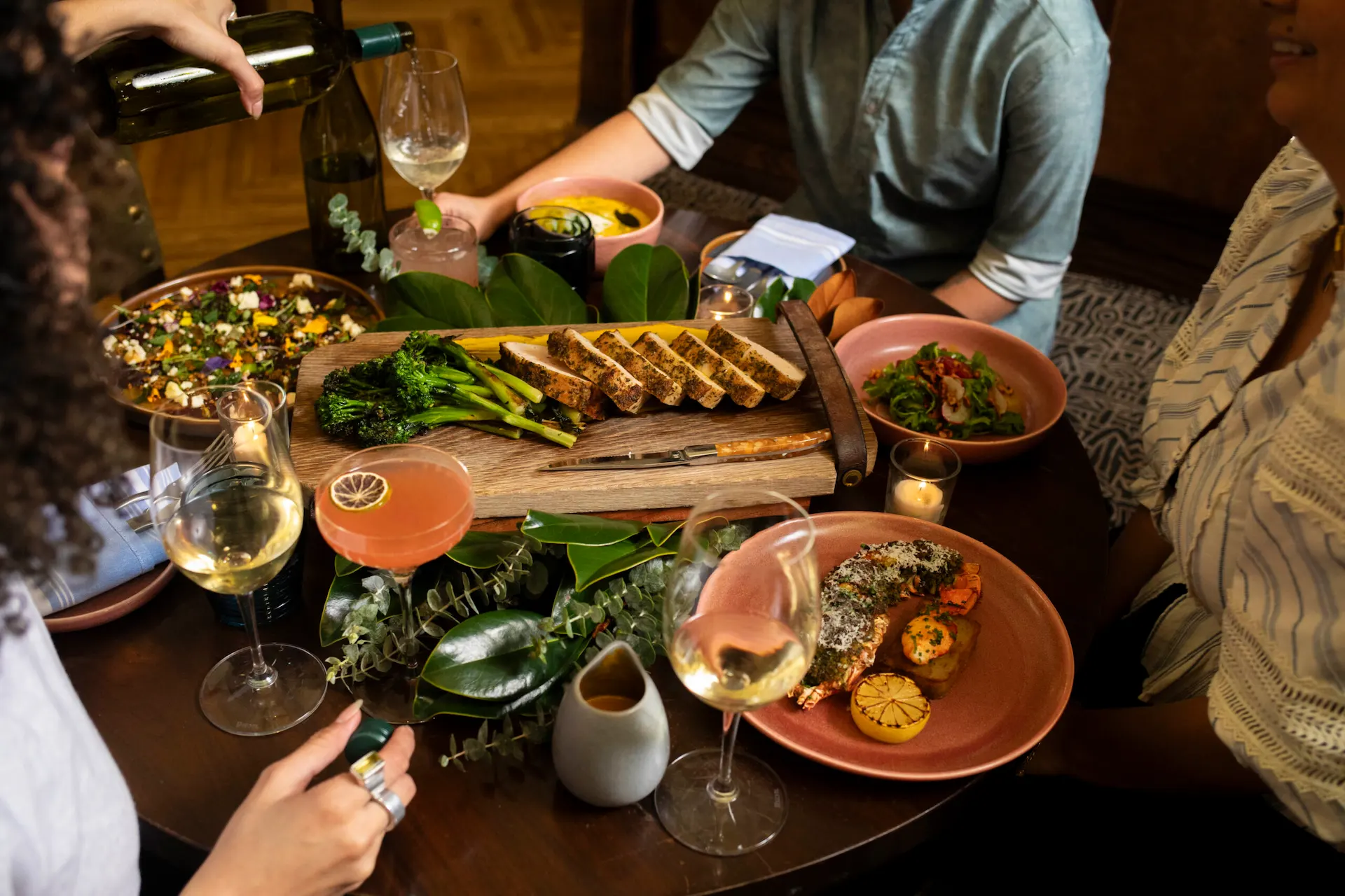 A cozy dinner gathering with friends around a rustic table filled with gourmet dishes, wine glasses, and candles.