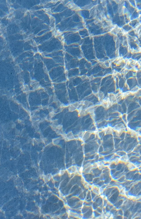 Sunlight creating rippling patterns across clear blue pool water.