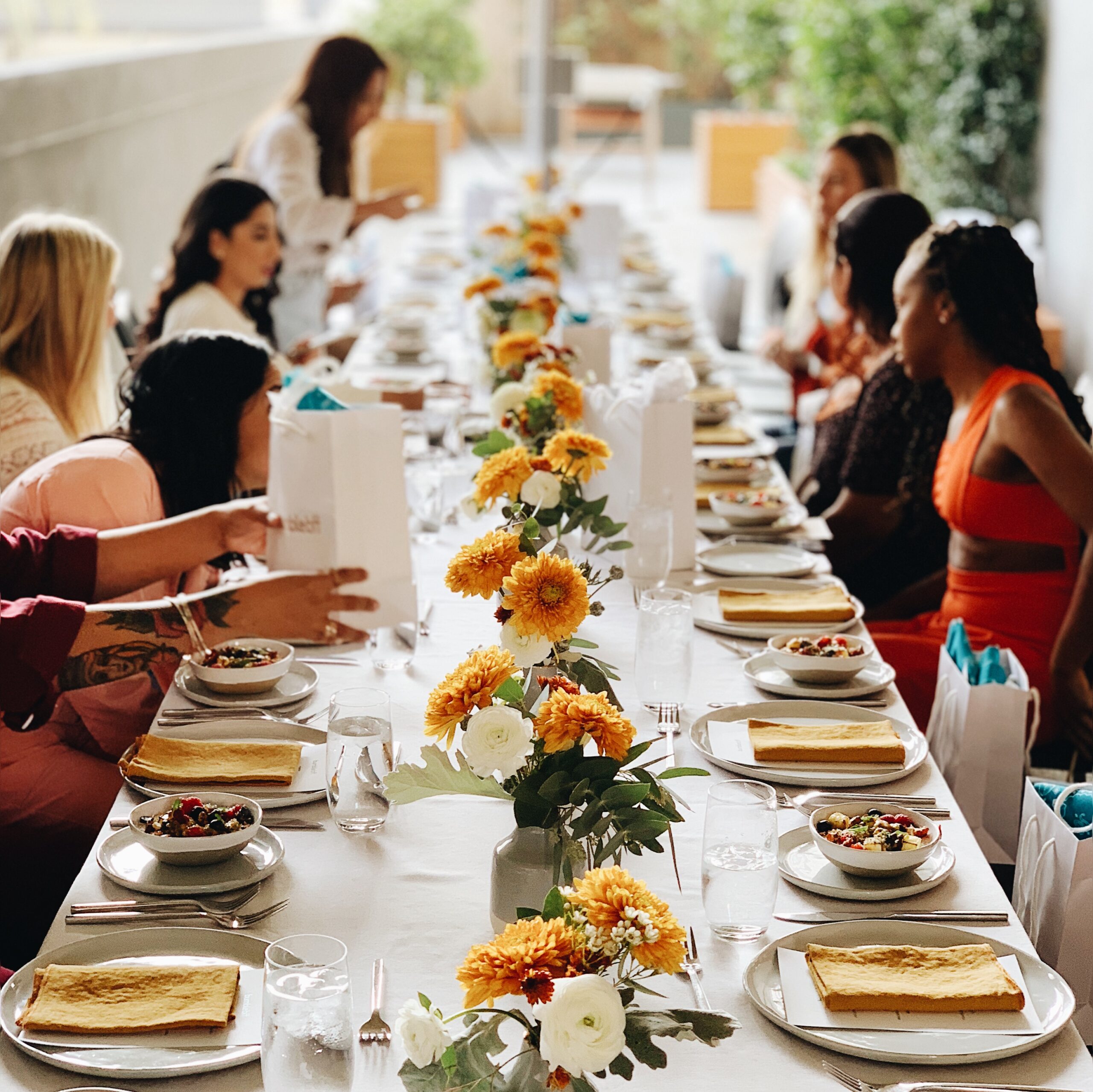 a long table set with food and flowers and people sitting on either side