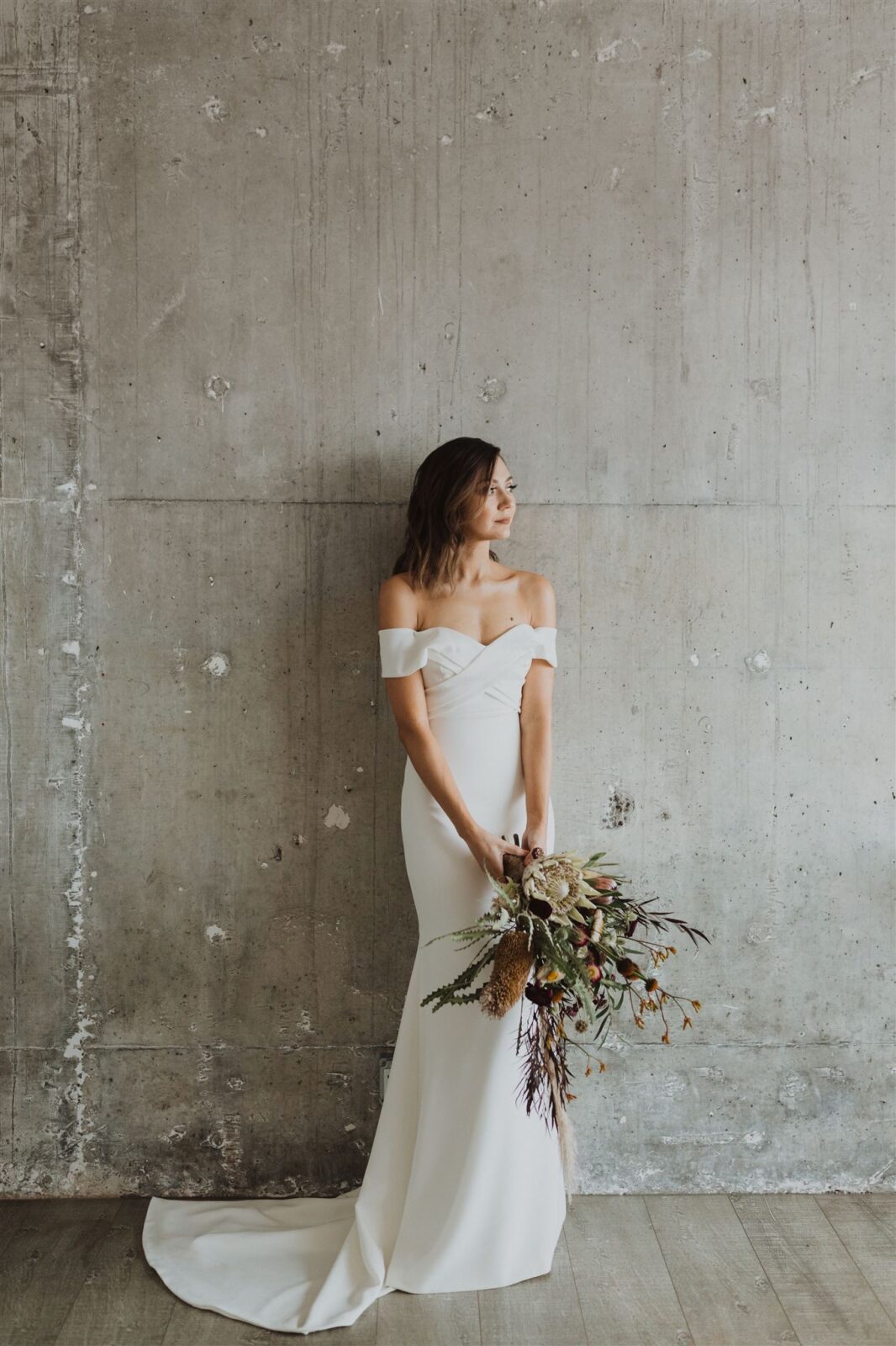 Bride in white dress posing against the grey wall while holding boutique