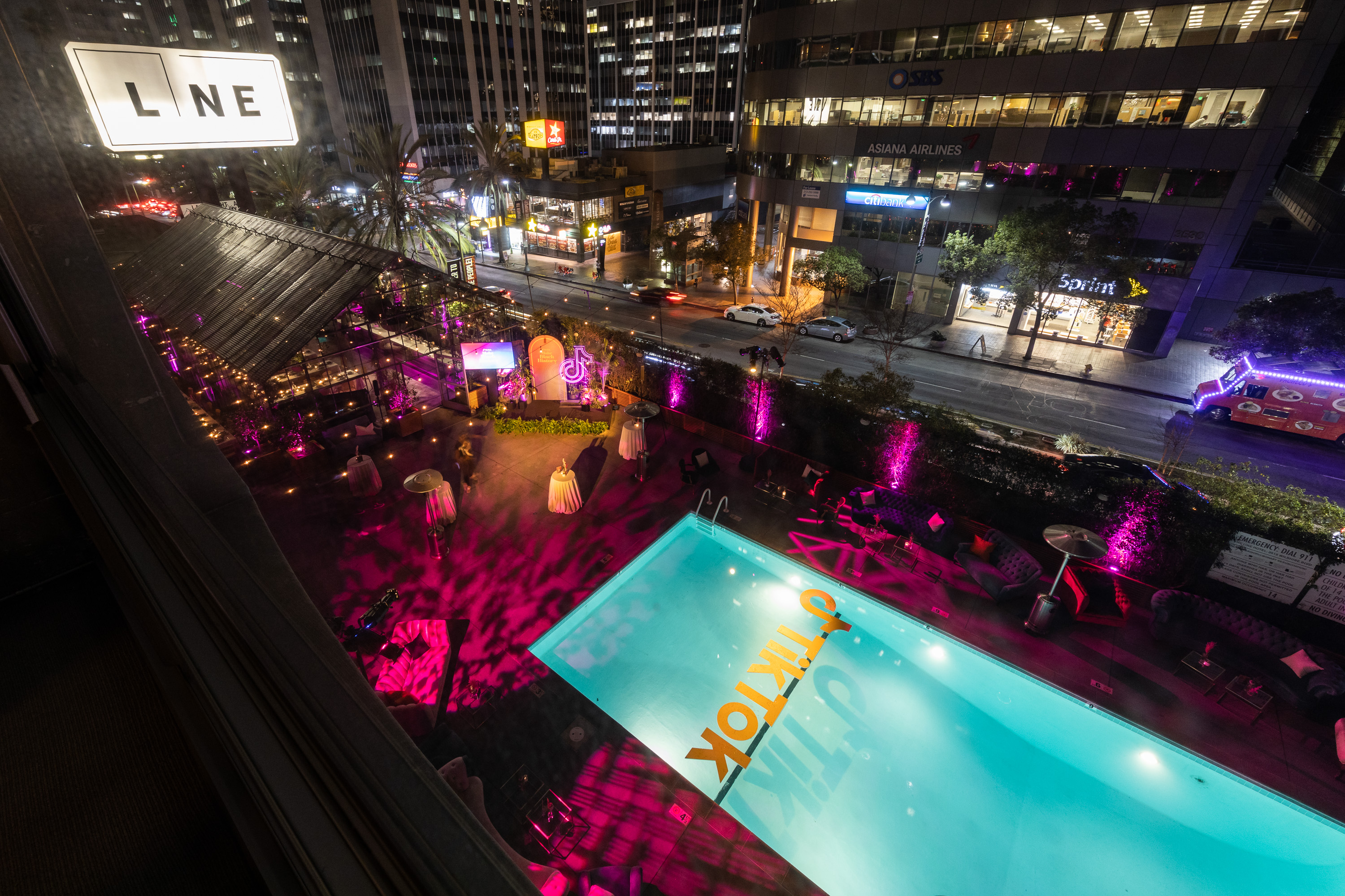 A nighttime aerial view of a hotel pool area with a city skyline in the background.