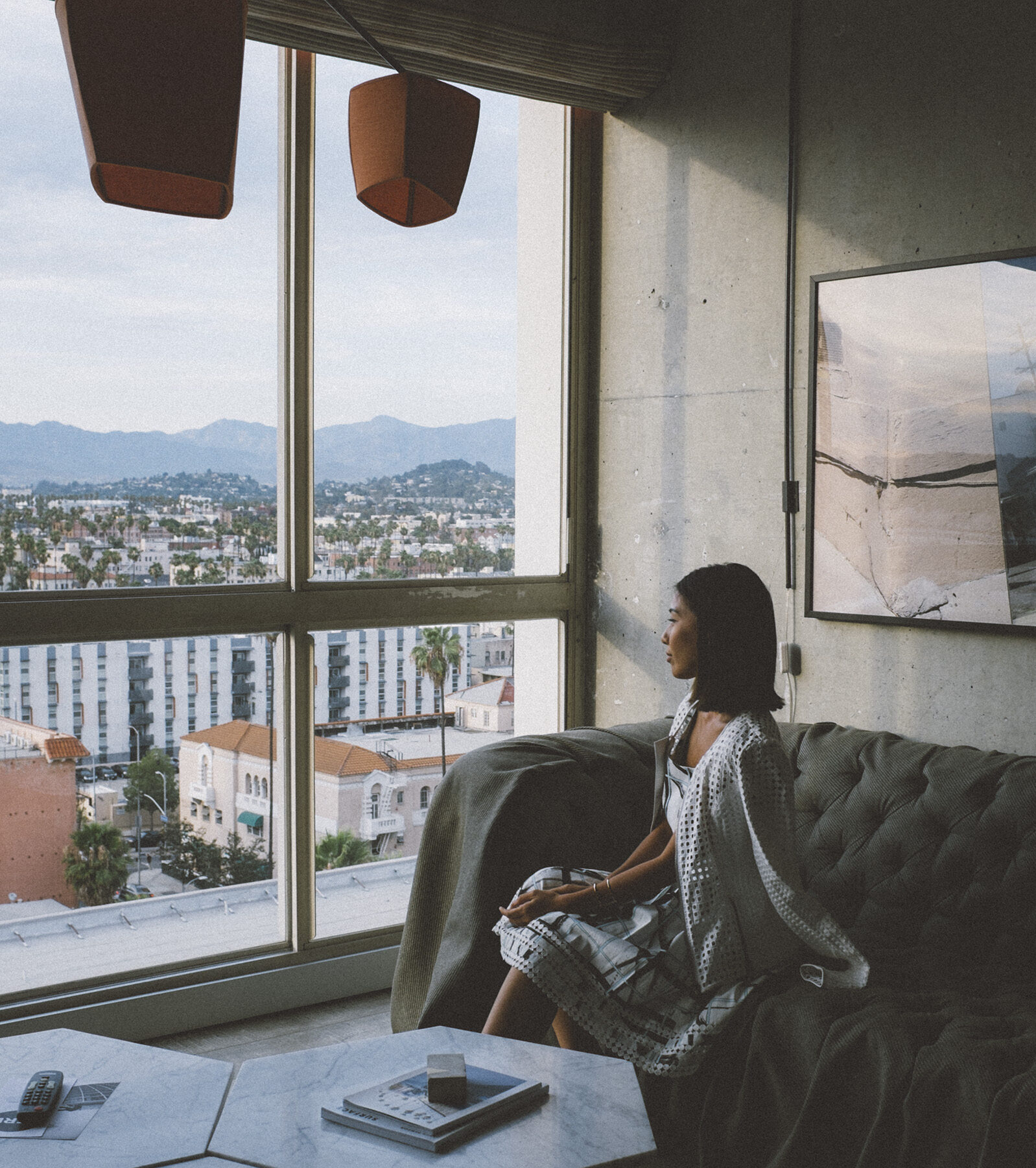 Woman sits on couch looking out a window to a view of hills in los angeles