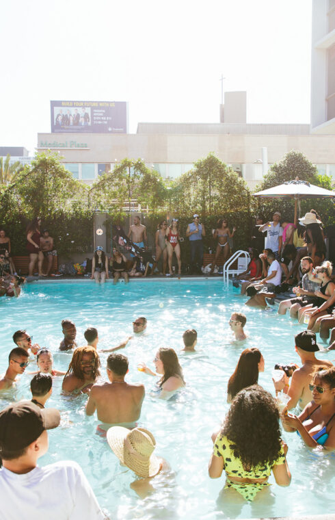 picture of a crowd at swimming pool with the background of plants and building