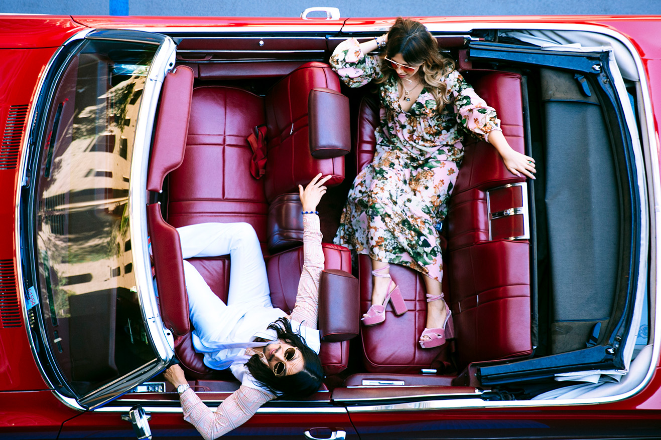 Two people lounging in a parked, red convertible car