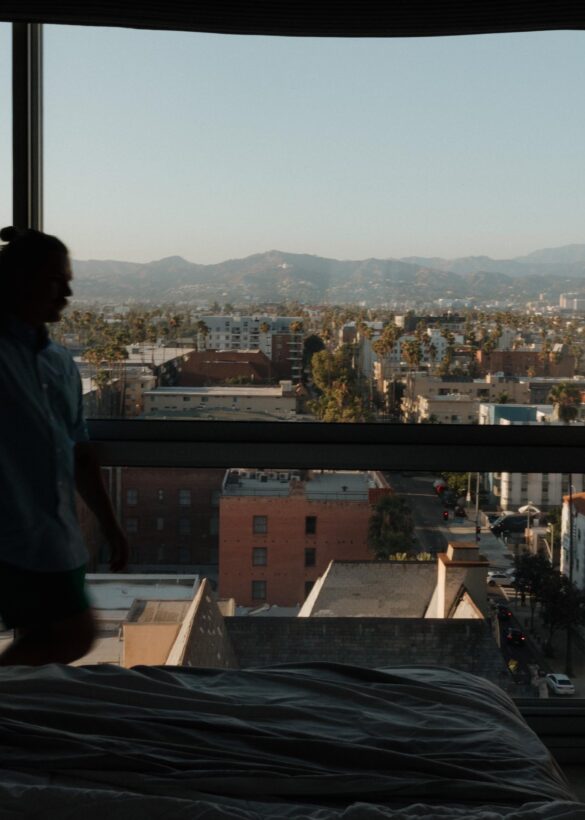 A man in shadow walks in front of a window with a view of the city and hills beyond