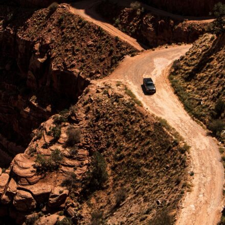 A car drives on a winding dirt road through steep, rocky terrain in Runyon Canyon.