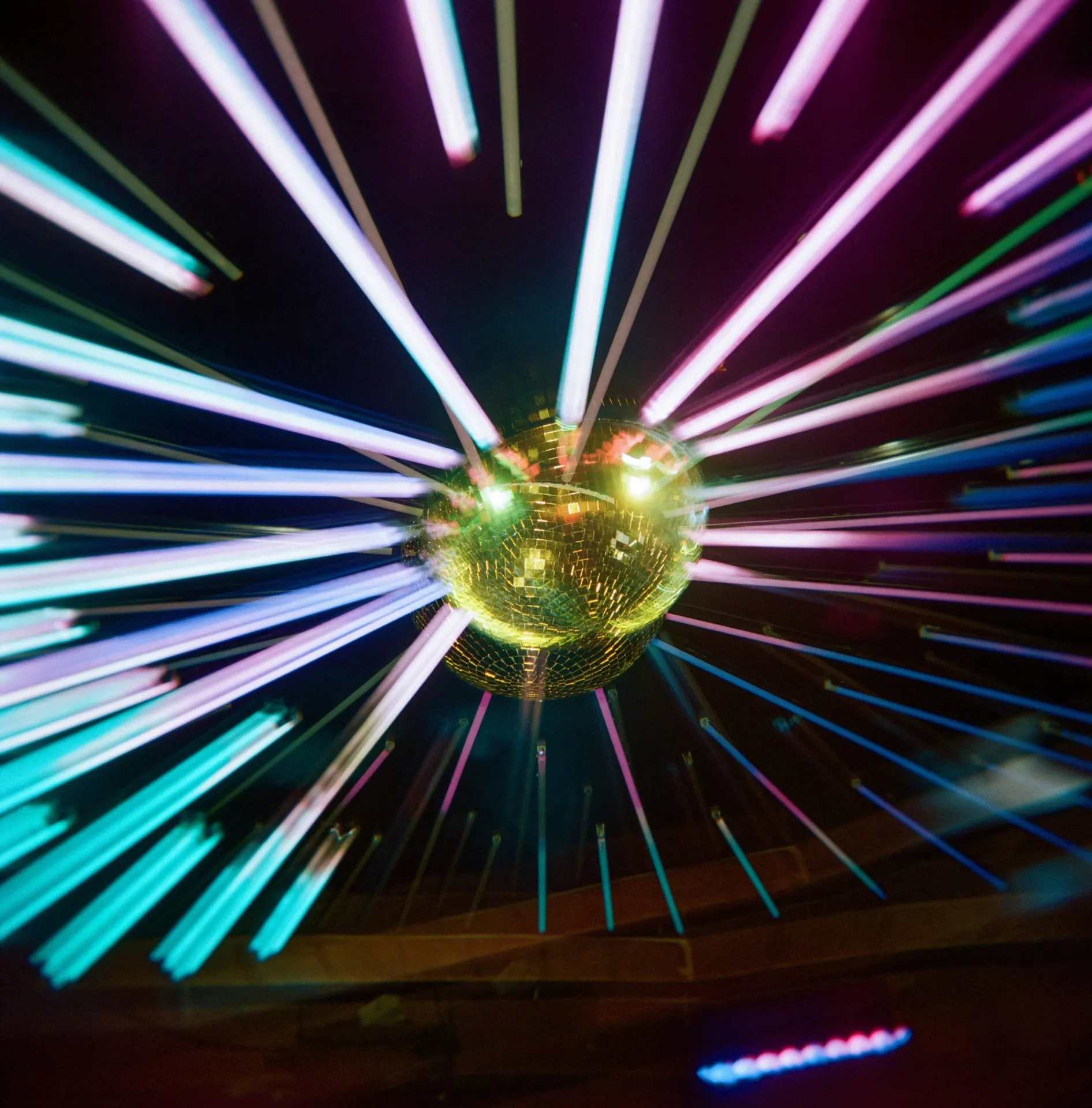 Golden disco ball radiates multicolored light streaks in vibrant party scene.