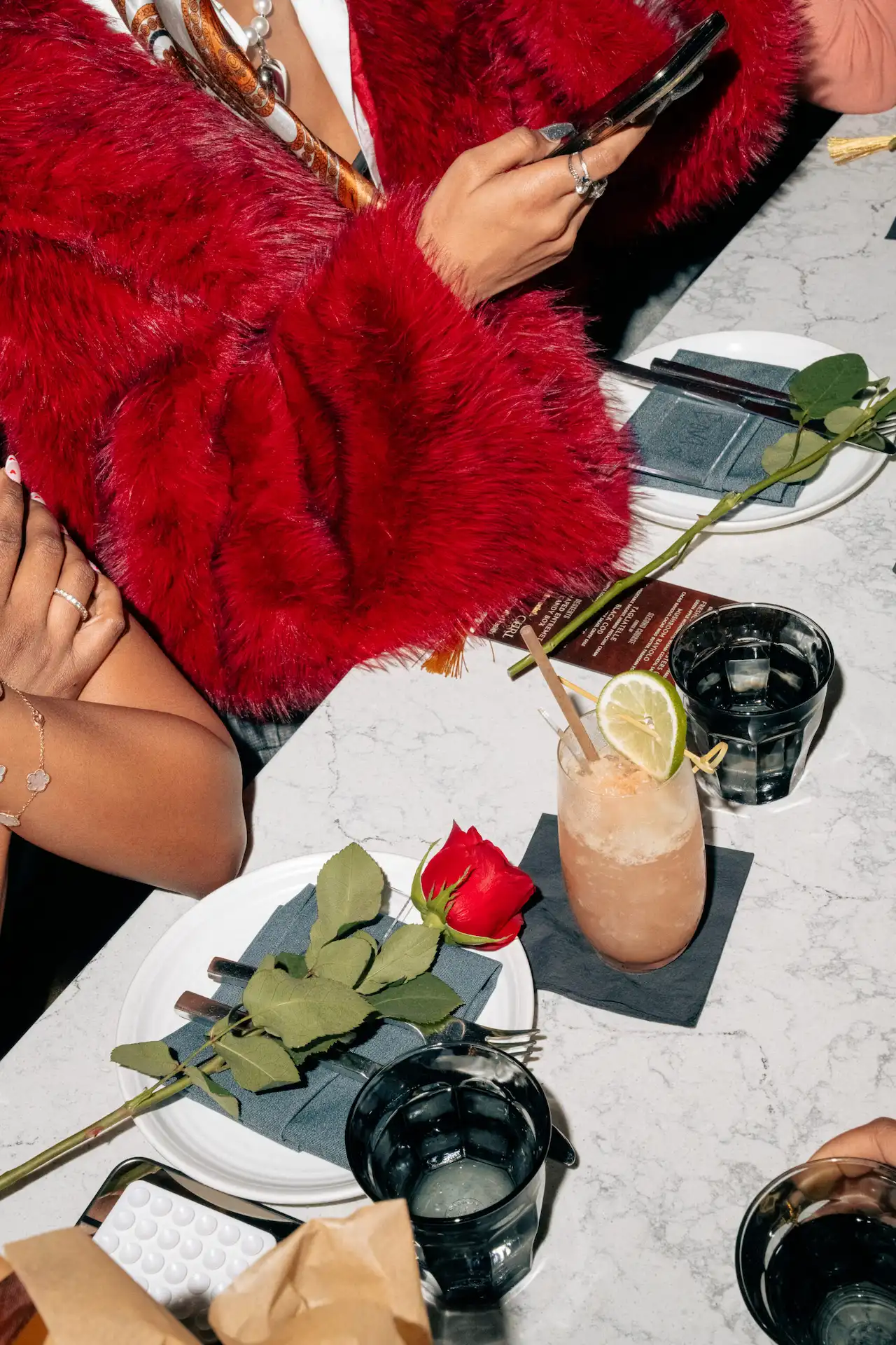 Cocktail and red rose on marble table during stylish dinner, with guests in bold fashion at The LINE.
