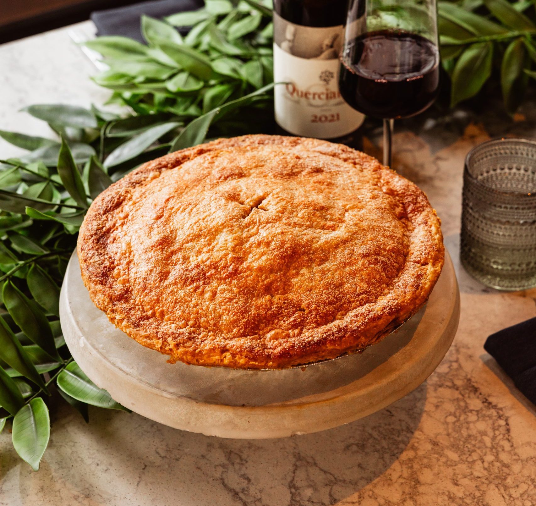 A pie on a table with a bottle of wine and a glass.