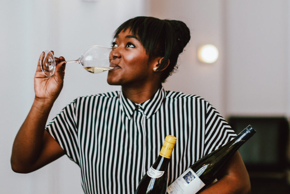 A lady wearing black and white shirt is drinking wine and hold two brown bottles too