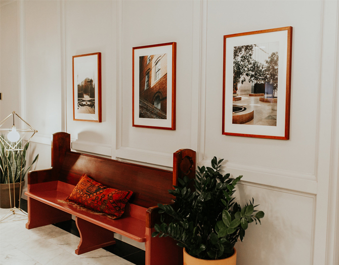 Picture of a red wooden seat with a pillow on it along with plant pots wall painting and lights