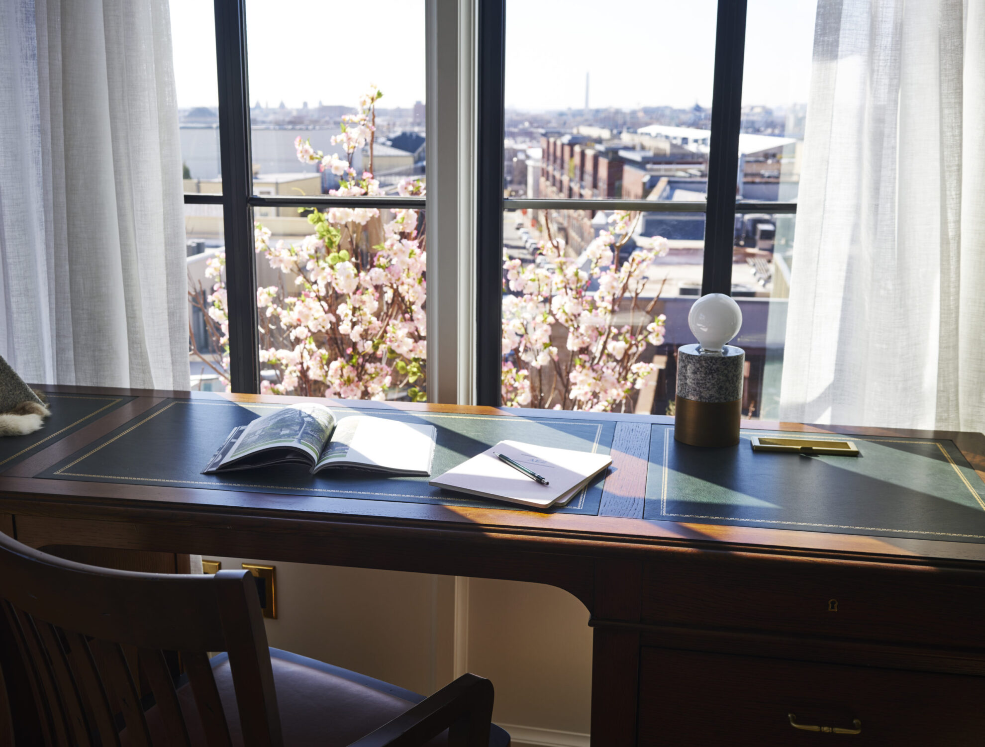 Picture of a study table with books and lamp on it along with city view from the window