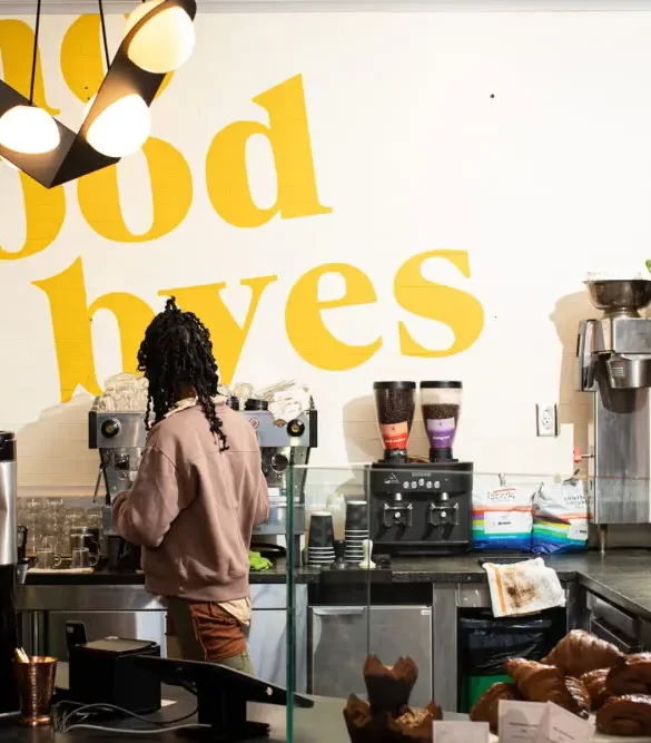 Picture of a kitchen where a person with curly hairs is looking towards the machine along with no good byes on wall