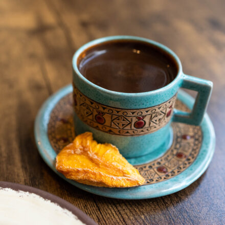 Coffee in a decorated blue cup with a piece of dried fruit on the saucer