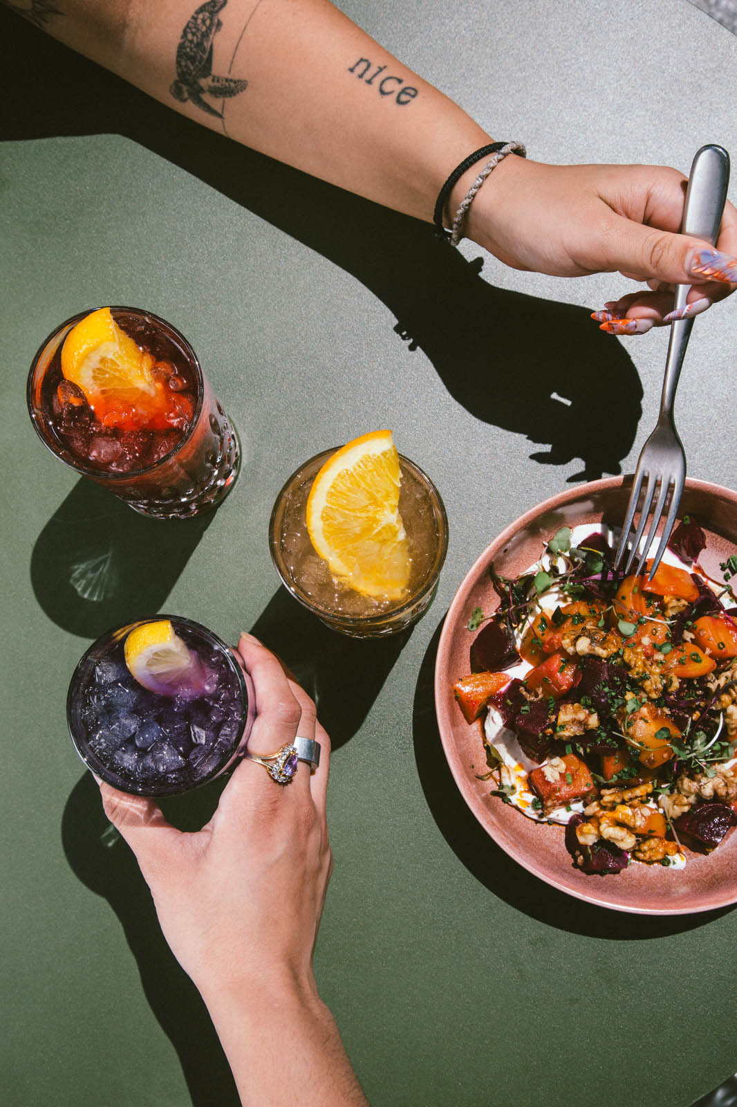 three glasses of drinks in purple, red, and brown, and a bowl of yogurt with fruit and granola