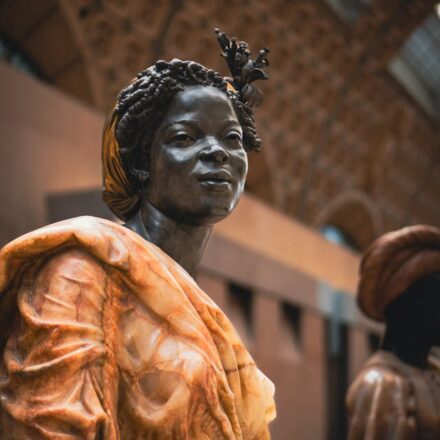 Statue of a woman in traditional attire, with intricate braids and a calm expression, in a museum setting.