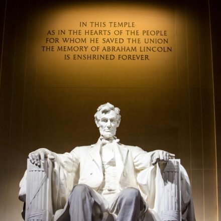 Statue of Abraham Lincoln seated at the Lincoln Memorial with an inscription on the wall behind him