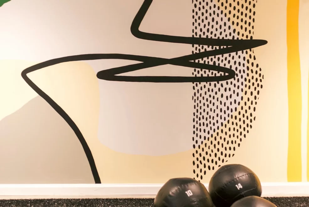 Three black medicine balls on gym floor with vibrant abstract mural of shapes and colors in background
