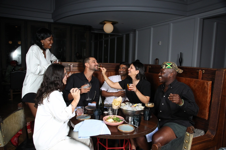 Group of six friends sharing oysters, chips, and drinks in a lively booth setting at The LINE.